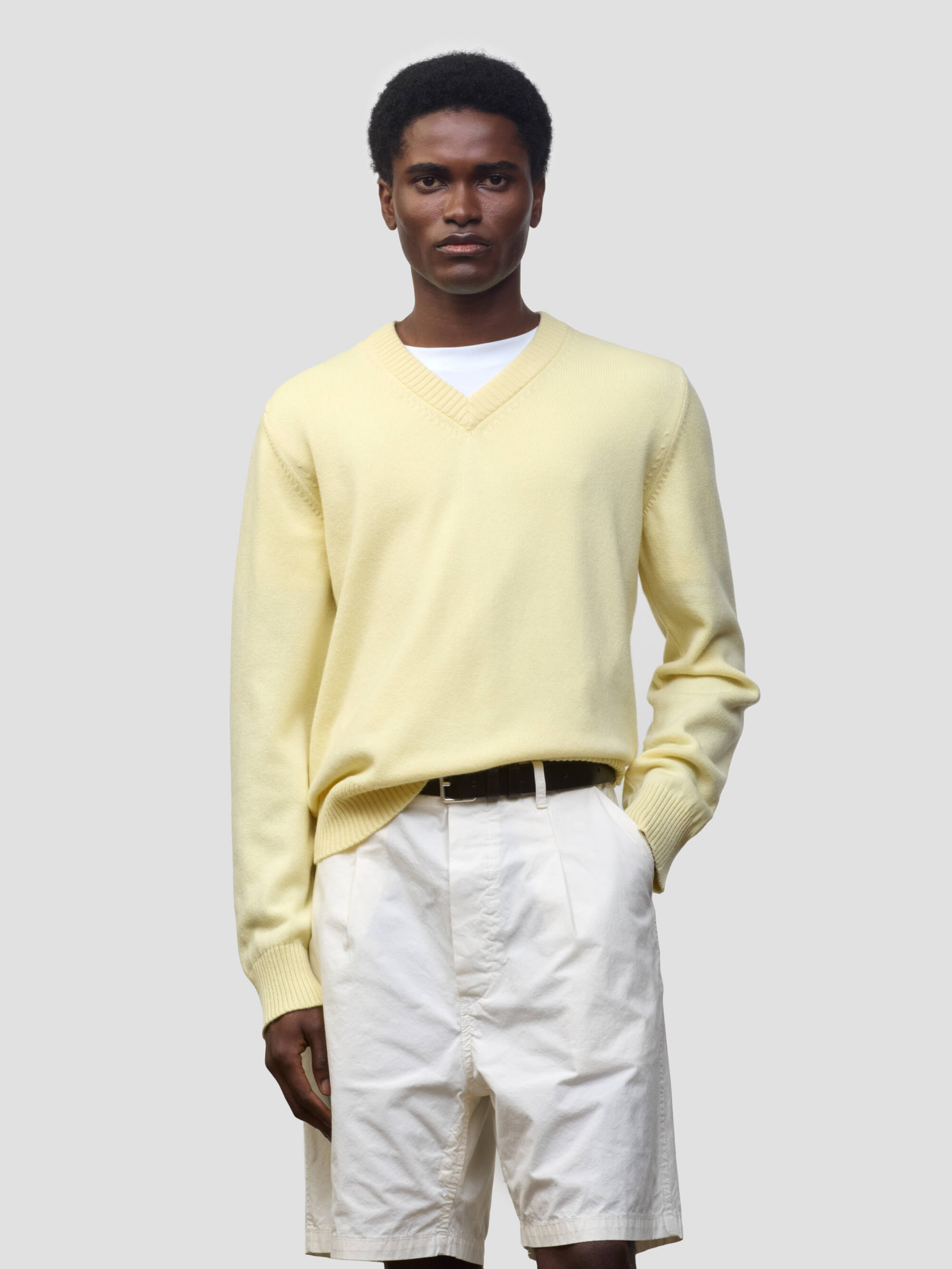 man wearing a light yellow v-neck sweater and white shorts on a grey background