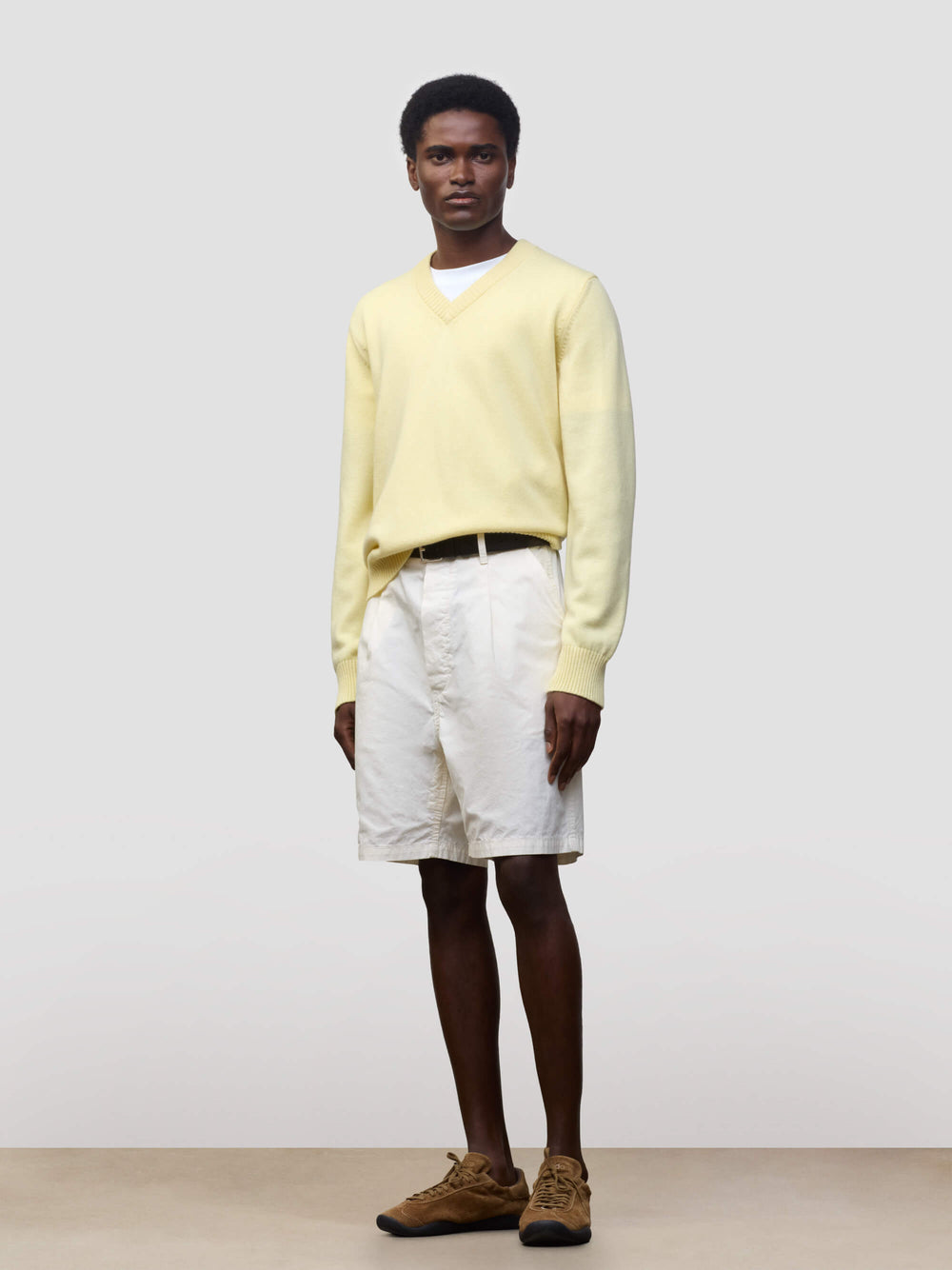 man wearing a light yellow v-neck sweater and white shorts on a grey background