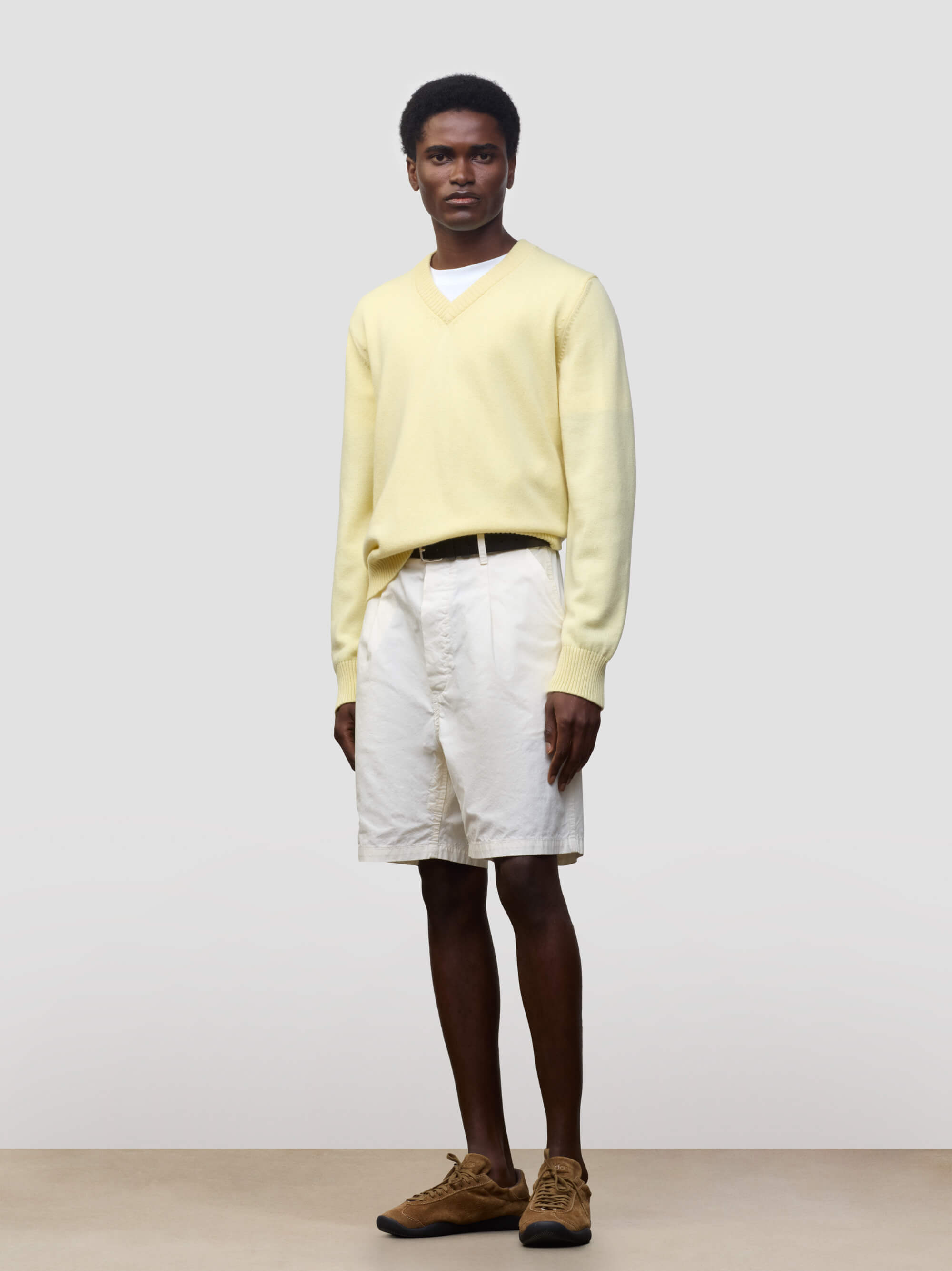 man wearing a light yellow v-neck sweater and white shorts on a grey background