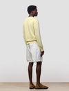 man wearing a light yellow v-neck sweater and white shorts on a grey background