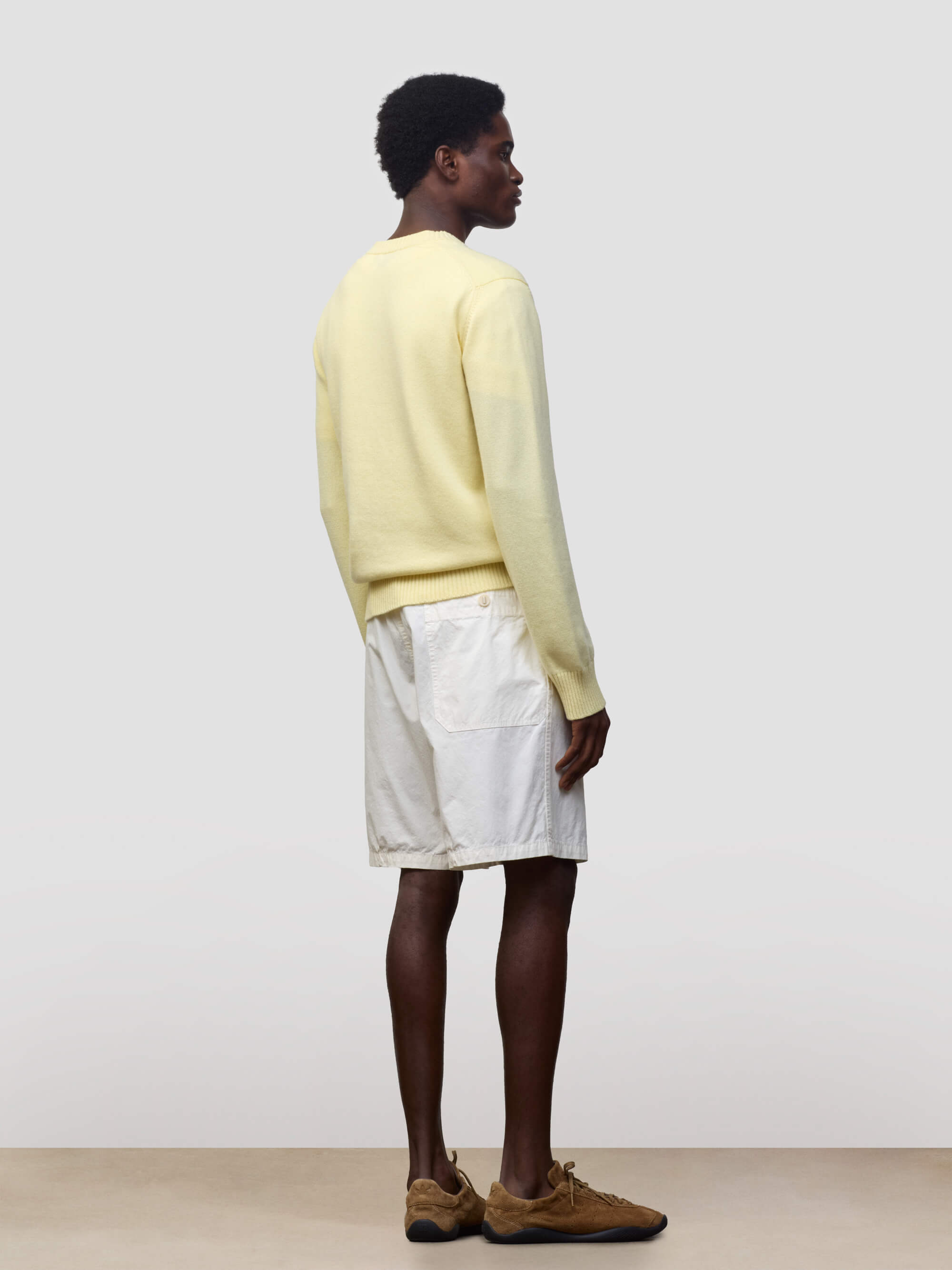 man wearing a light yellow v-neck sweater and white shorts on a grey background
