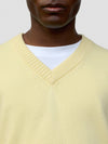 close up of a man wearing a light yellow v-neck sweater on a grey background
