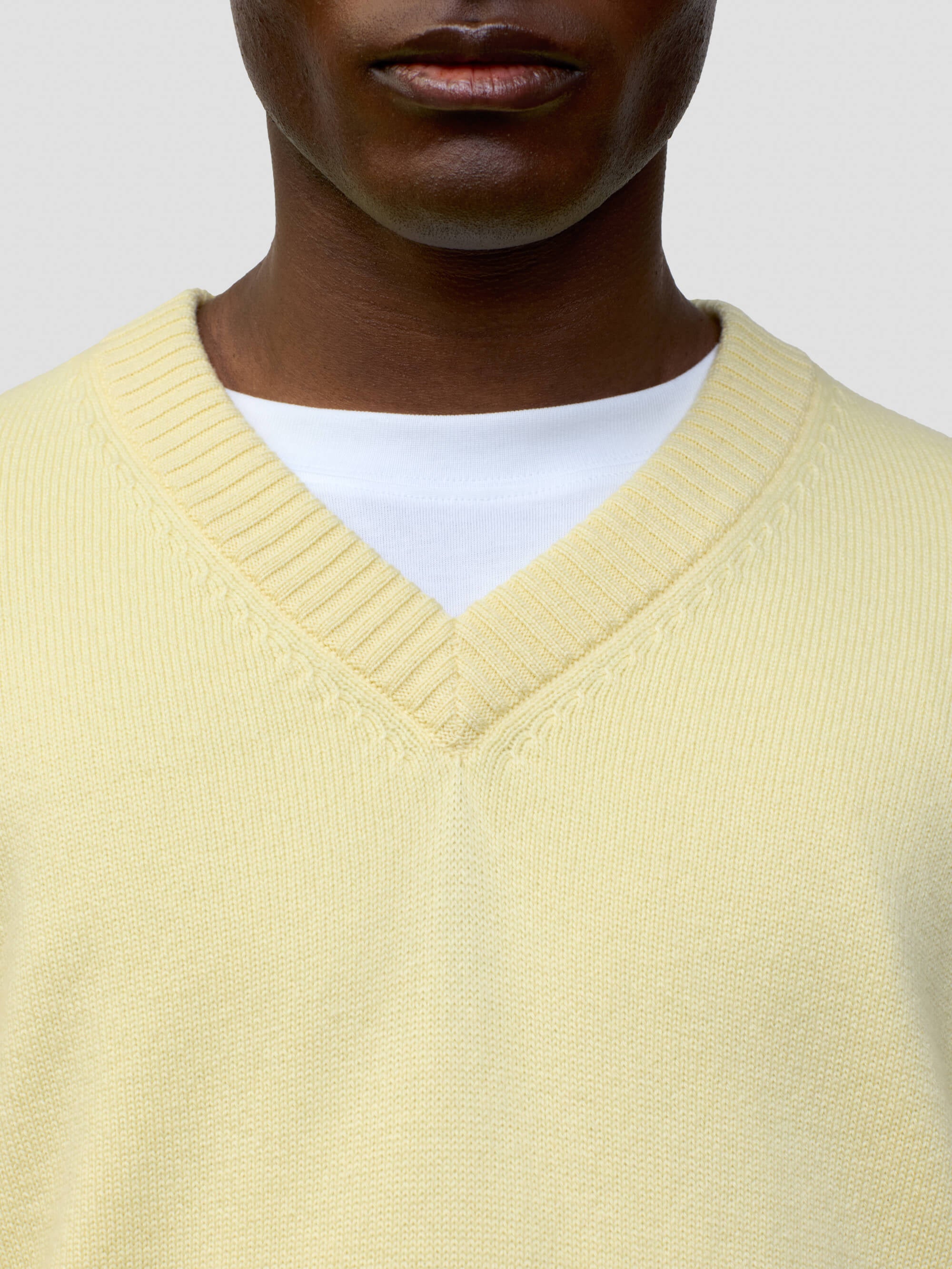 close up of a man wearing a light yellow v-neck sweater on a grey background