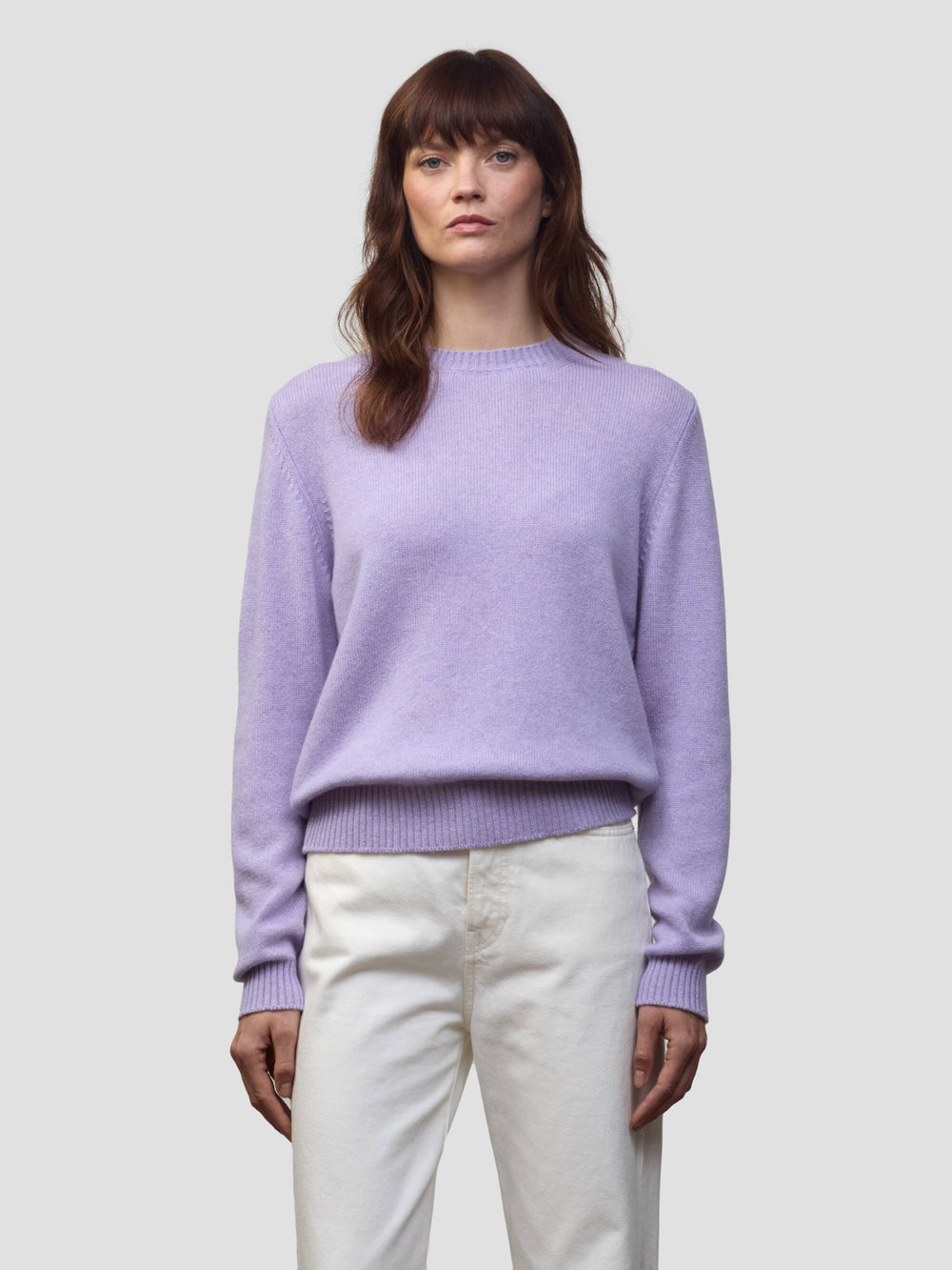 Woman wearing a light purple cashmere sweater and white pants against a plain background
