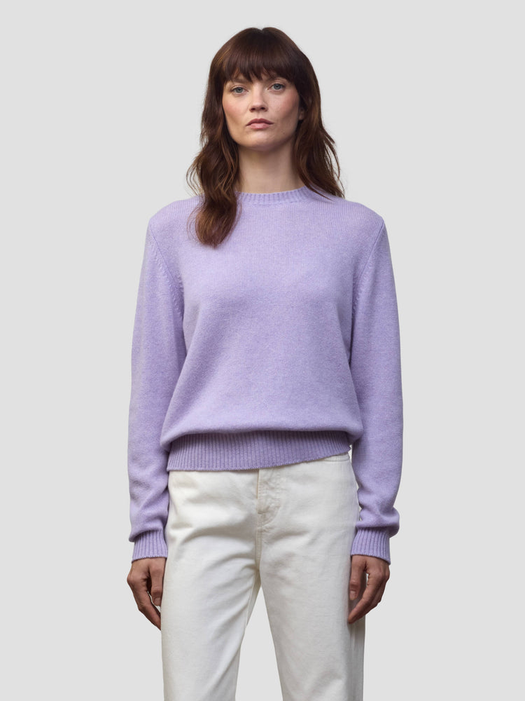 Woman wearing a light purple cashmere sweater and white pants against a plain background