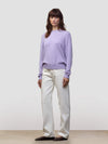 Woman wearing a light purple cashmere sweater and white pants against a plain background