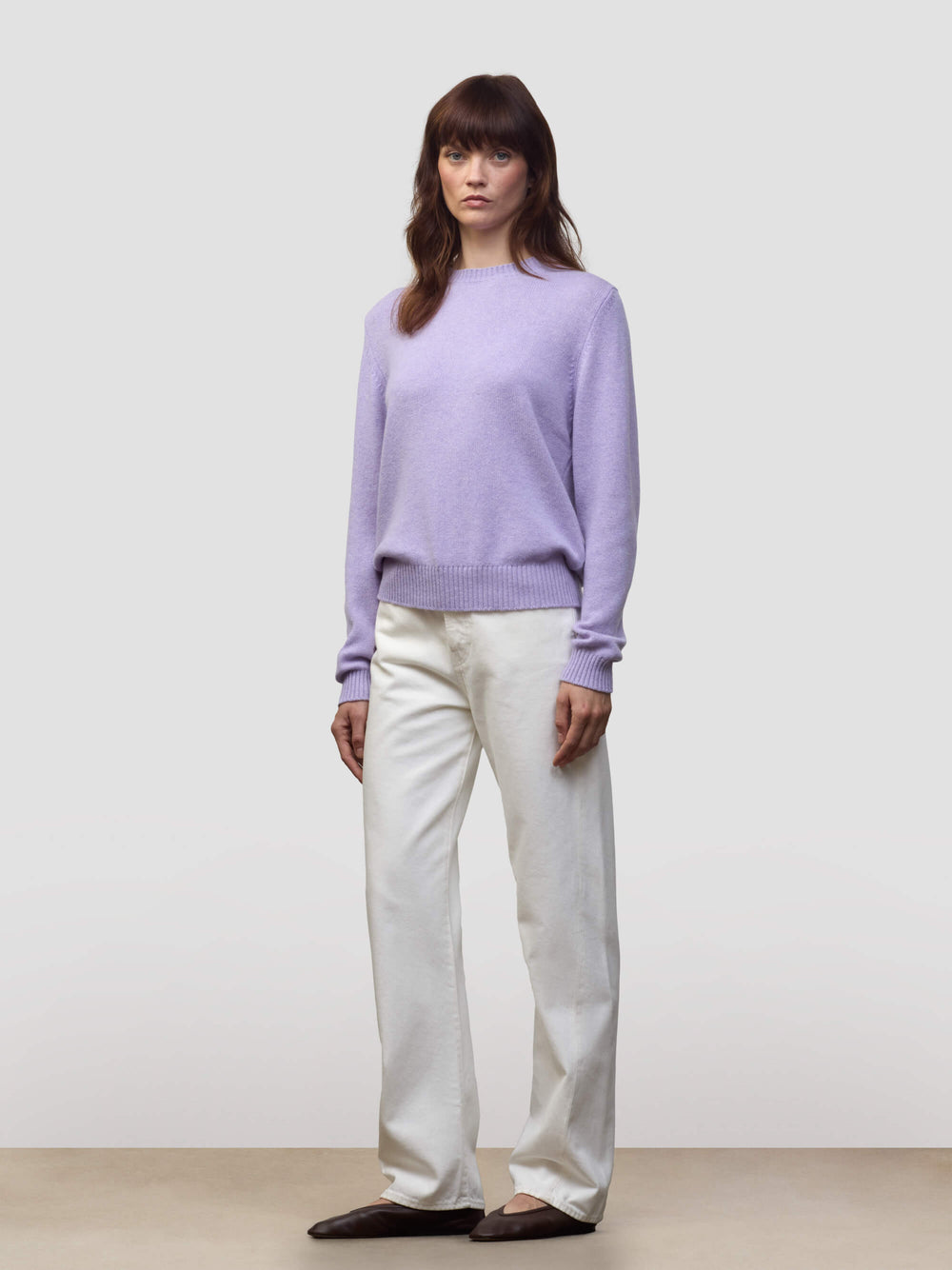 Woman wearing a light purple cashmere sweater and white pants against a plain background