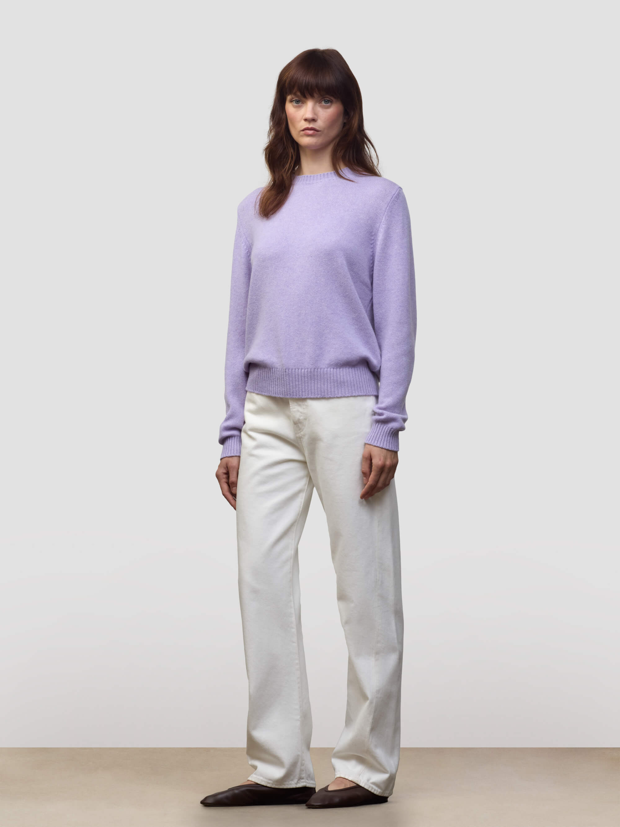Woman wearing a light purple cashmere sweater and white pants against a plain background