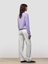 Woman wearing a light purple cashmere sweater and white pants against a plain background