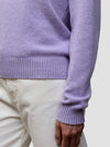 Woman wearing a light purple cashmere sweater and white pants against a plain background