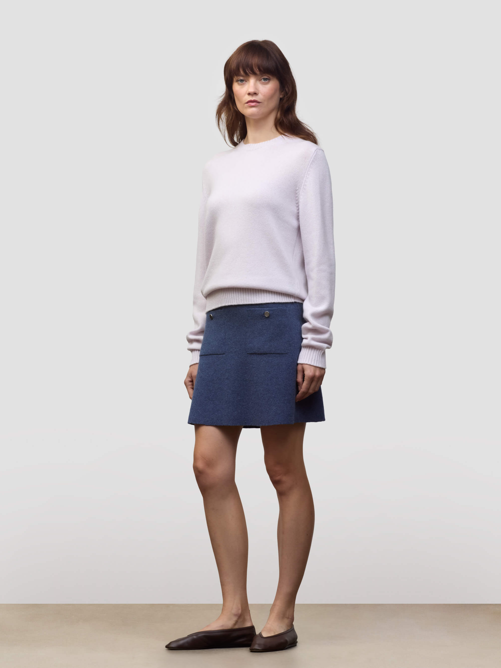 Woman wearing a light pink cashmere sweater and blue cashmere skirt against a plain background