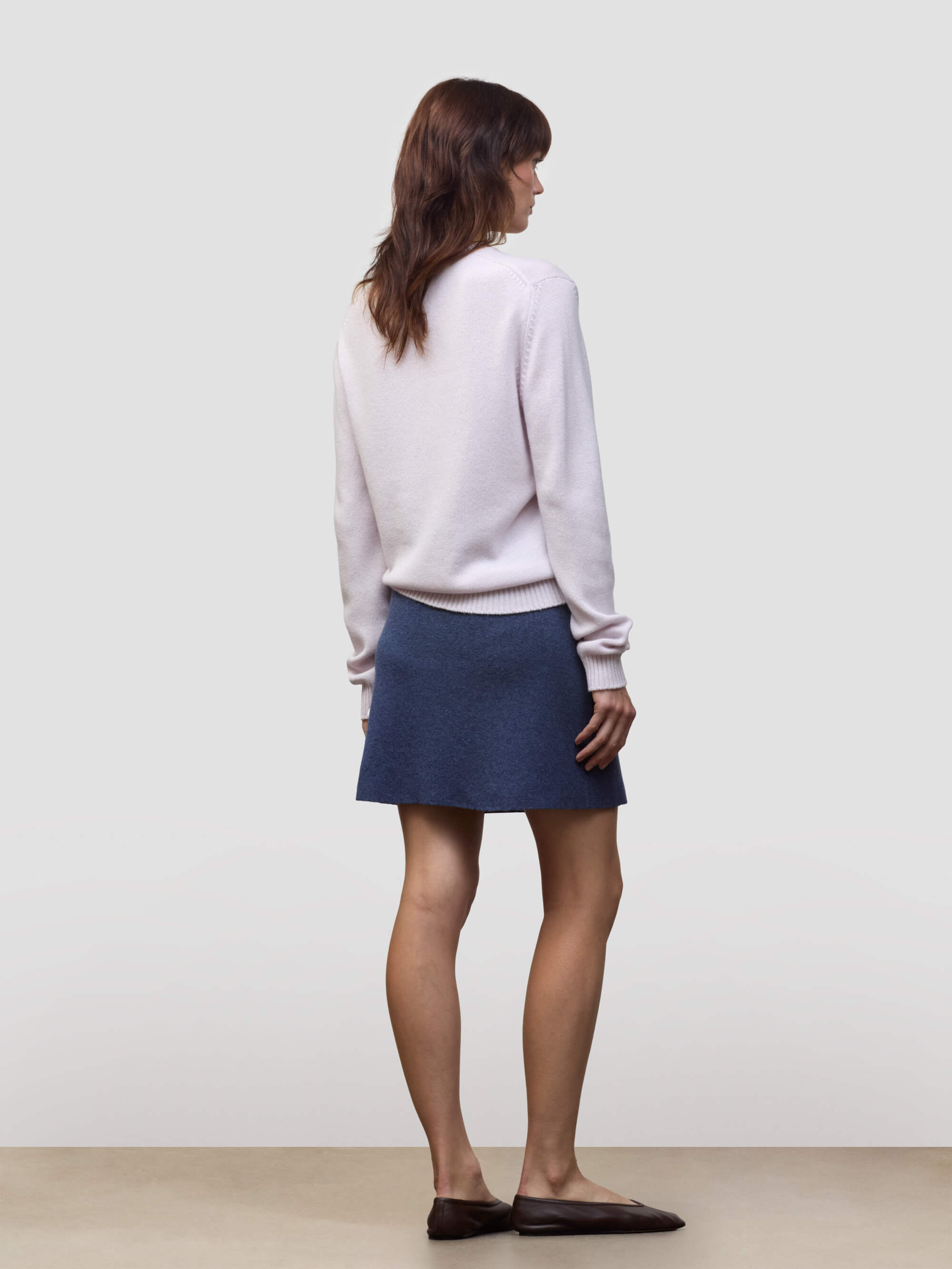 Woman wearing a light pink cashmere sweater and blue cashmere skirt against a plain background