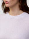 Close-up of a woman wearing a light pink sweater against a white background