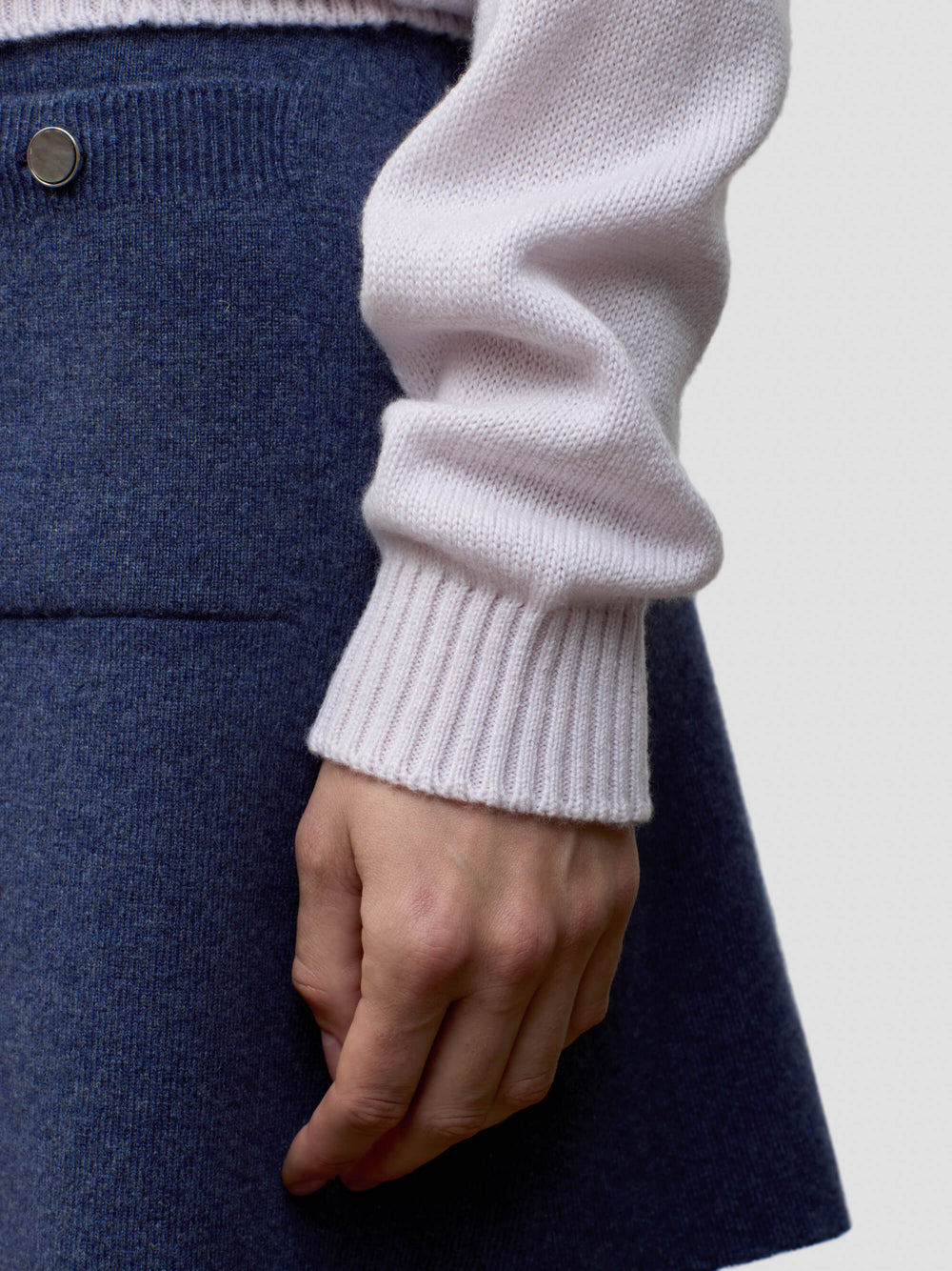 Close-up of a woman wearing a light pink cashmere sweater and dark blue cashmere skirt.