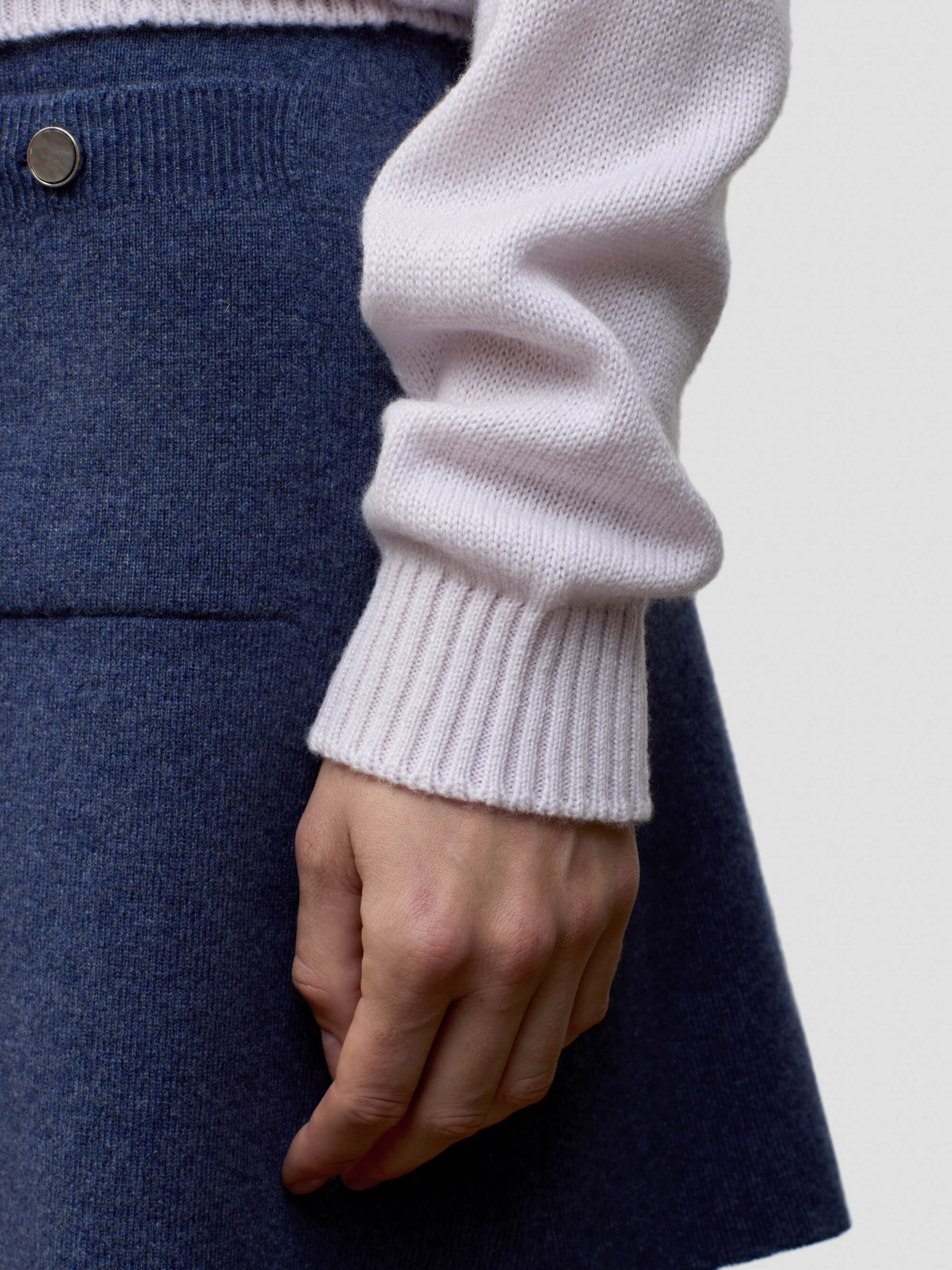 Close-up of a woman wearing a light pink cashmere sweater and dark blue cashmere skirt.
