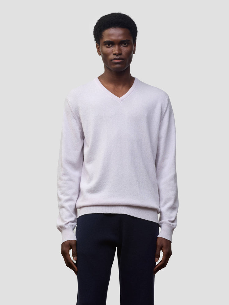 man wearing a light pink cashmere v-neck sweater and navy trousers on a grey background