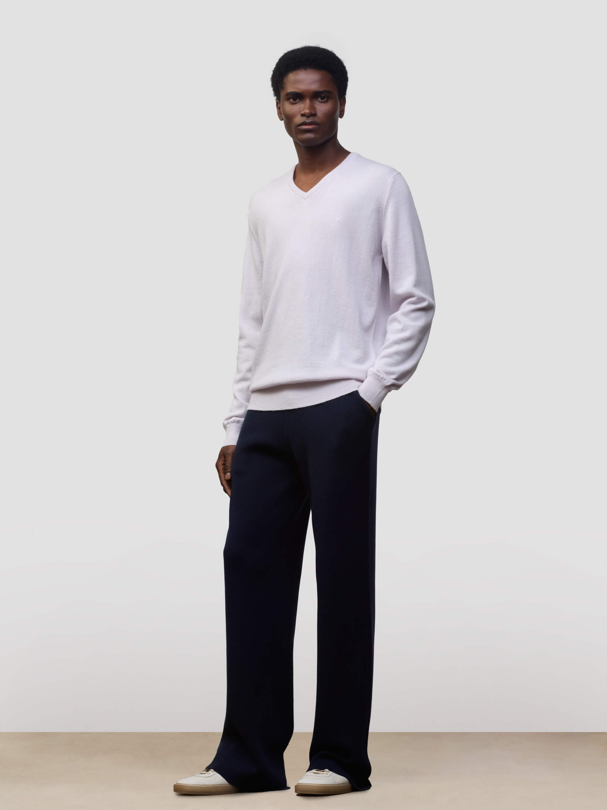 man wearing a light pink cashmere v-neck sweater and navy trousers on a grey background