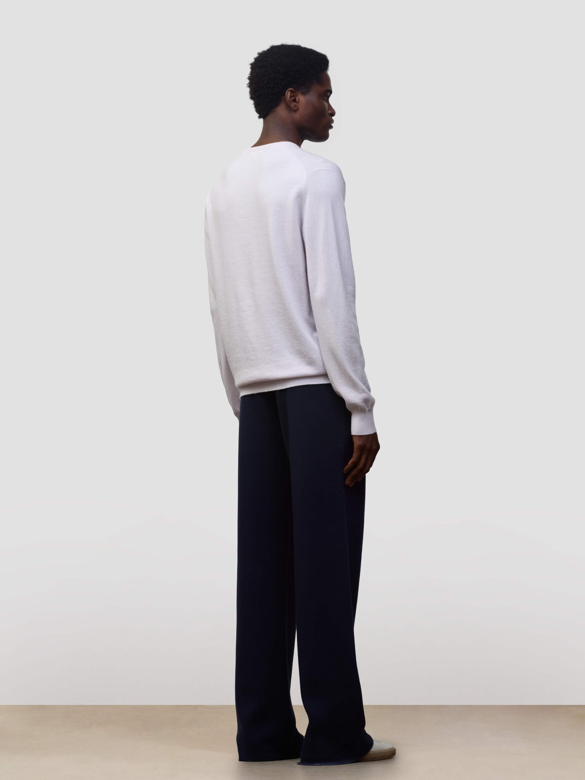 man wearing a light pink cashmere v-neck sweater and navy trousers on a grey background