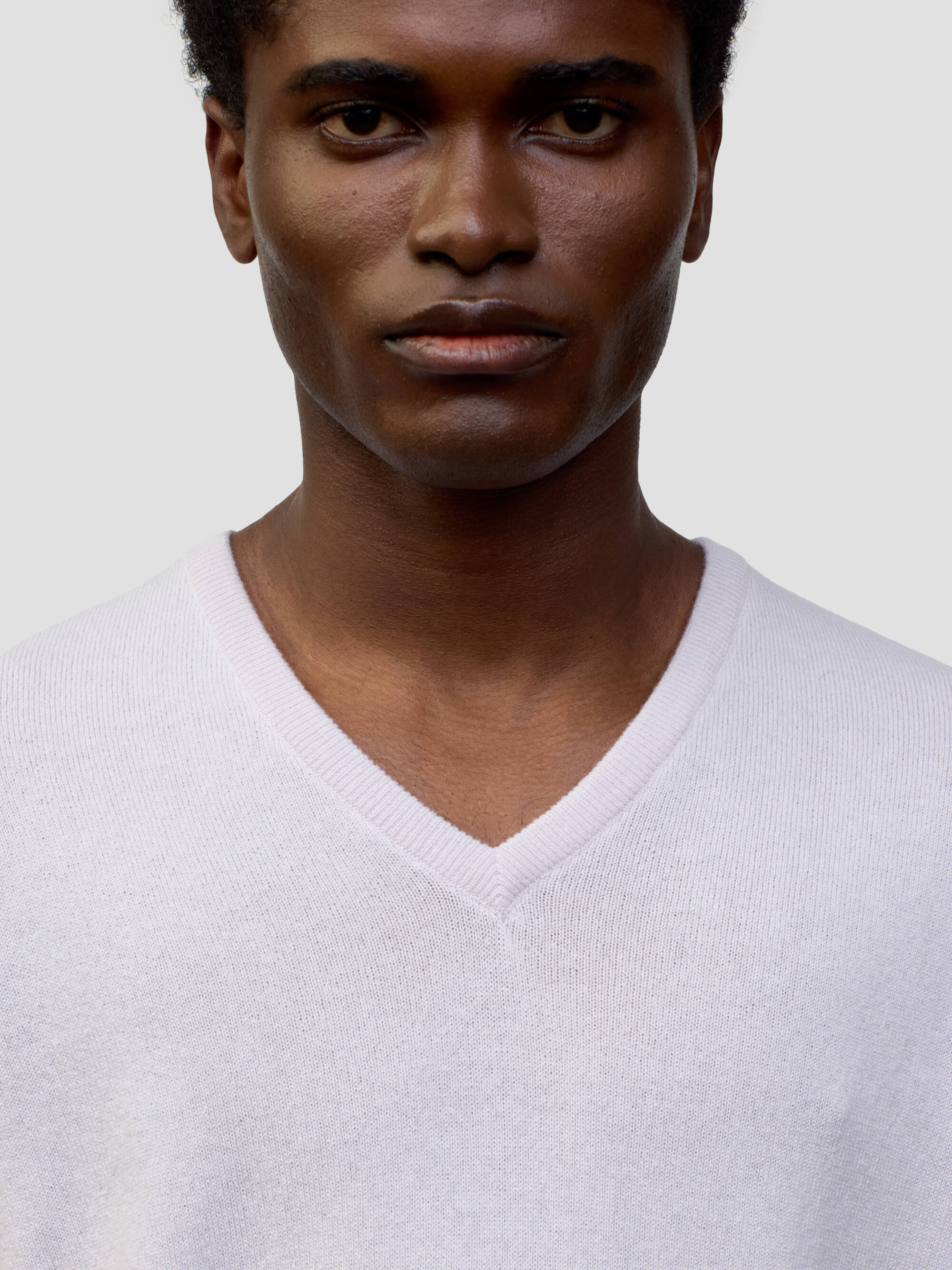 man wearing a light pink cashmere v-neck sweater on a grey background