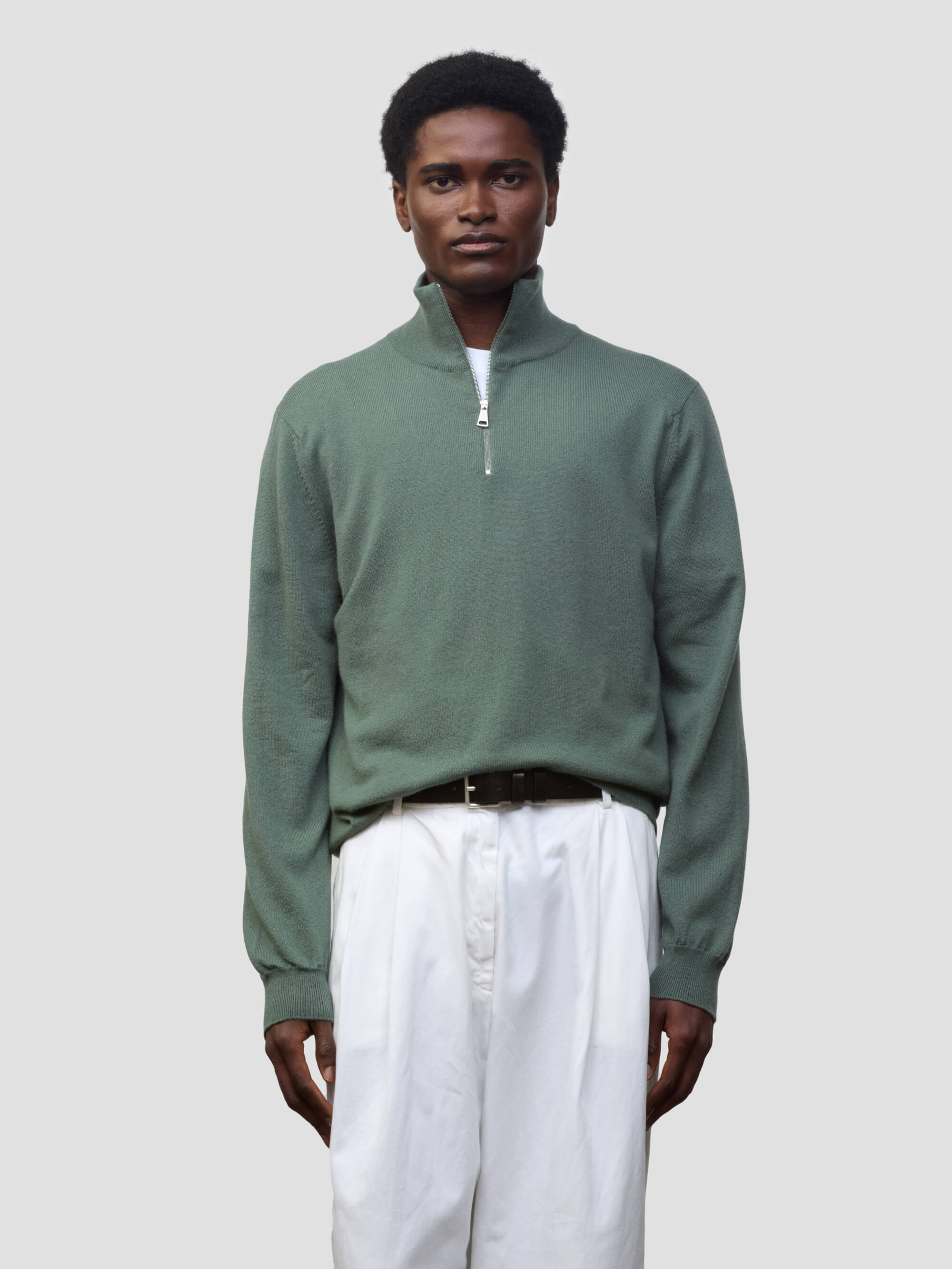 man wearing a green quarter-zip cashmere sweater and white pants on a plain background
