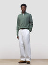 man wearing a green quarter-zip cashmere sweater and white pants on a plain background