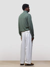 man wearing a green quarter-zip cashmere sweater and white pants on a plain background