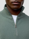 man wearing a green quarter-zip cashmere sweater and white pants on a plain background