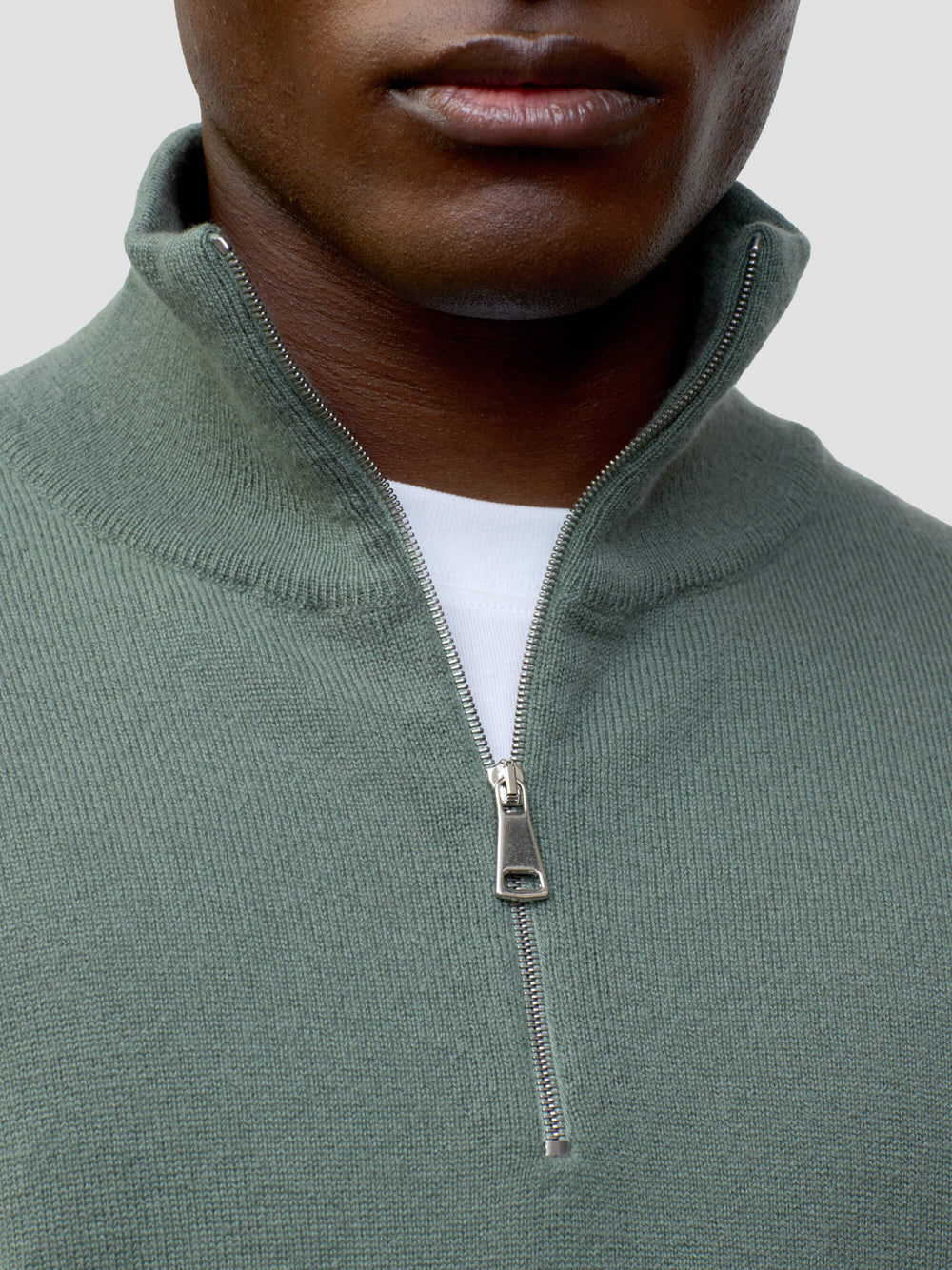 man wearing a green quarter-zip cashmere sweater and white pants on a plain background
