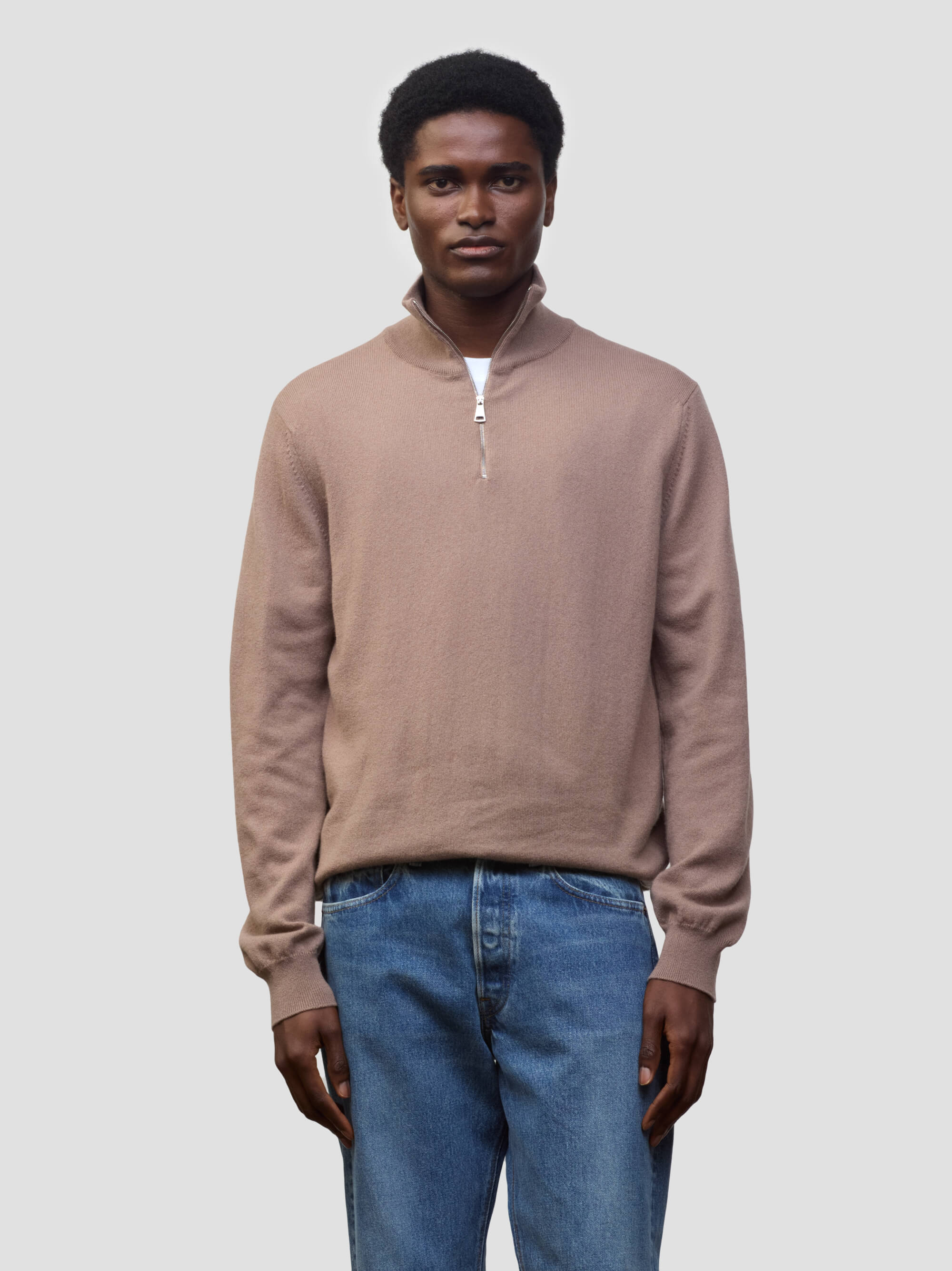 Man wearing a brown sweater and blue jeans against a plain background