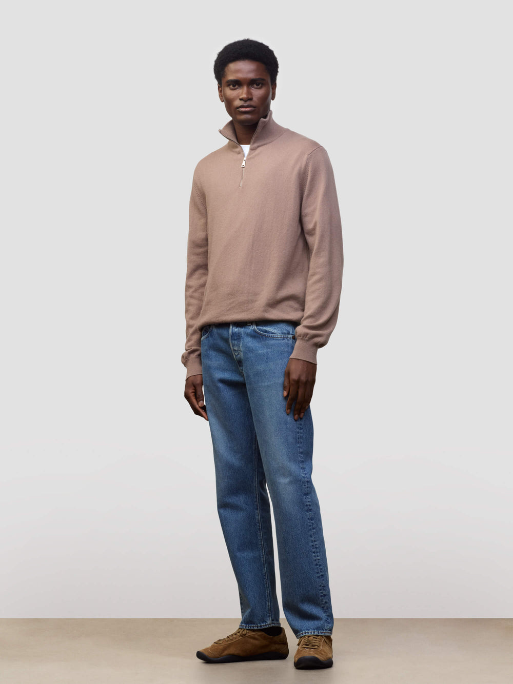 Man wearing a brown sweater and blue jeans against a plain background