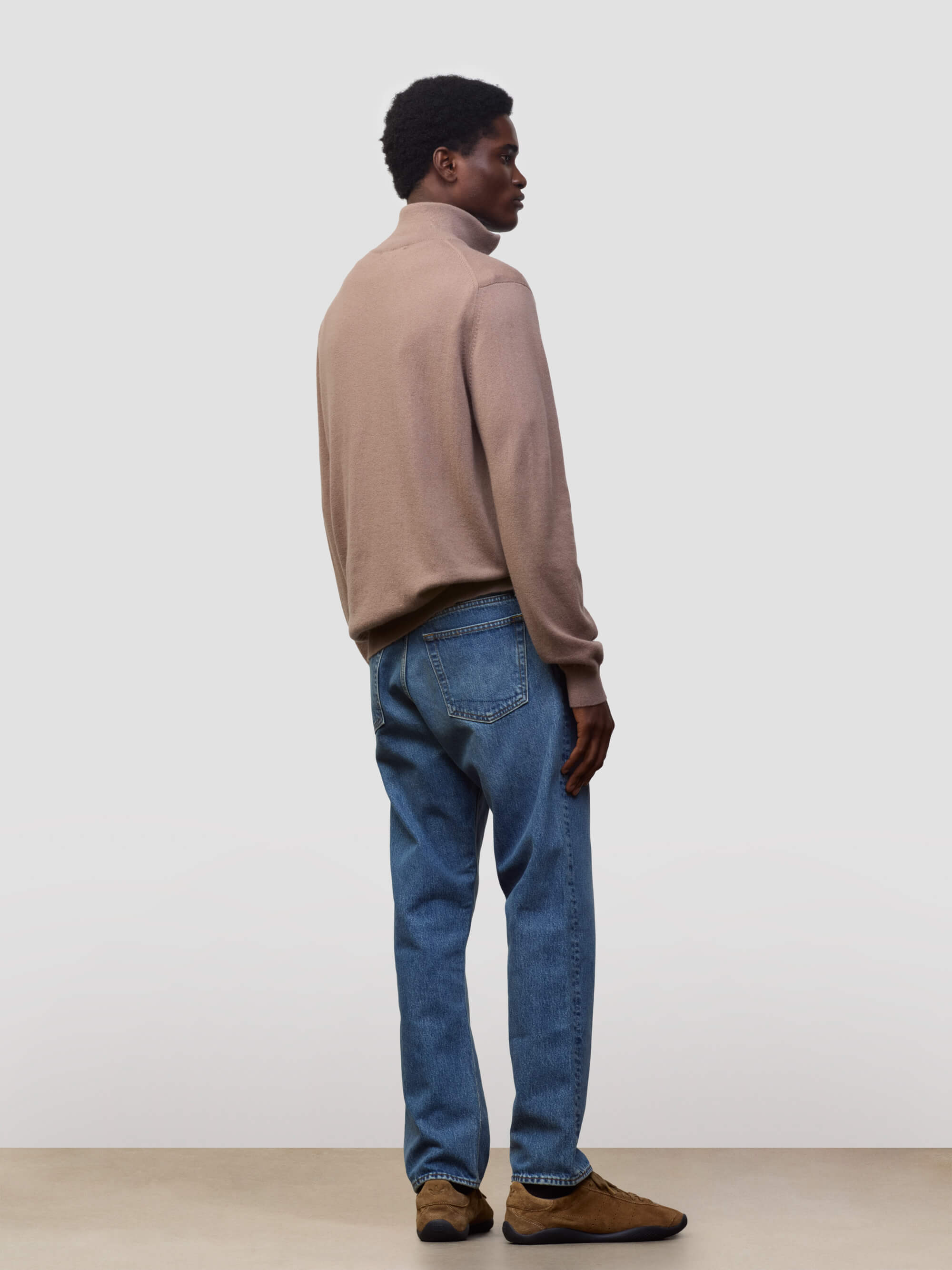 Man wearing a brown sweater and blue jeans against a plain background