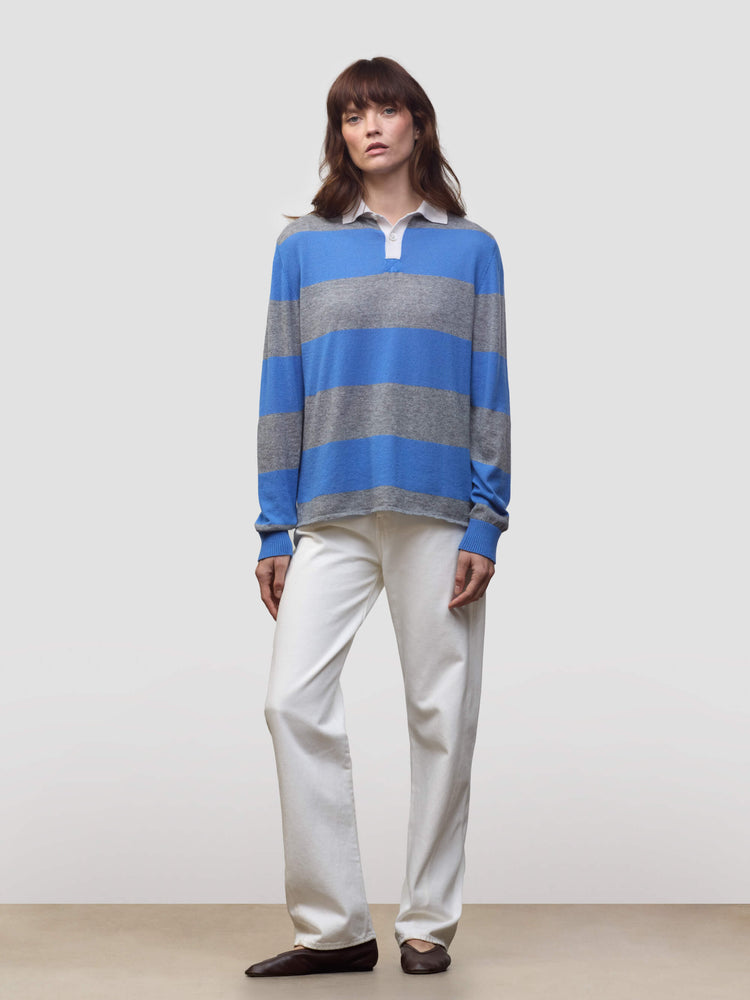 woman wearing a blue and grey striped cashmere rugby shirt and white trousers on a grey background