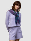 woman wearing a cable knit purple sweater and matching shorts with a check purple, green and blue scarf on a grey background