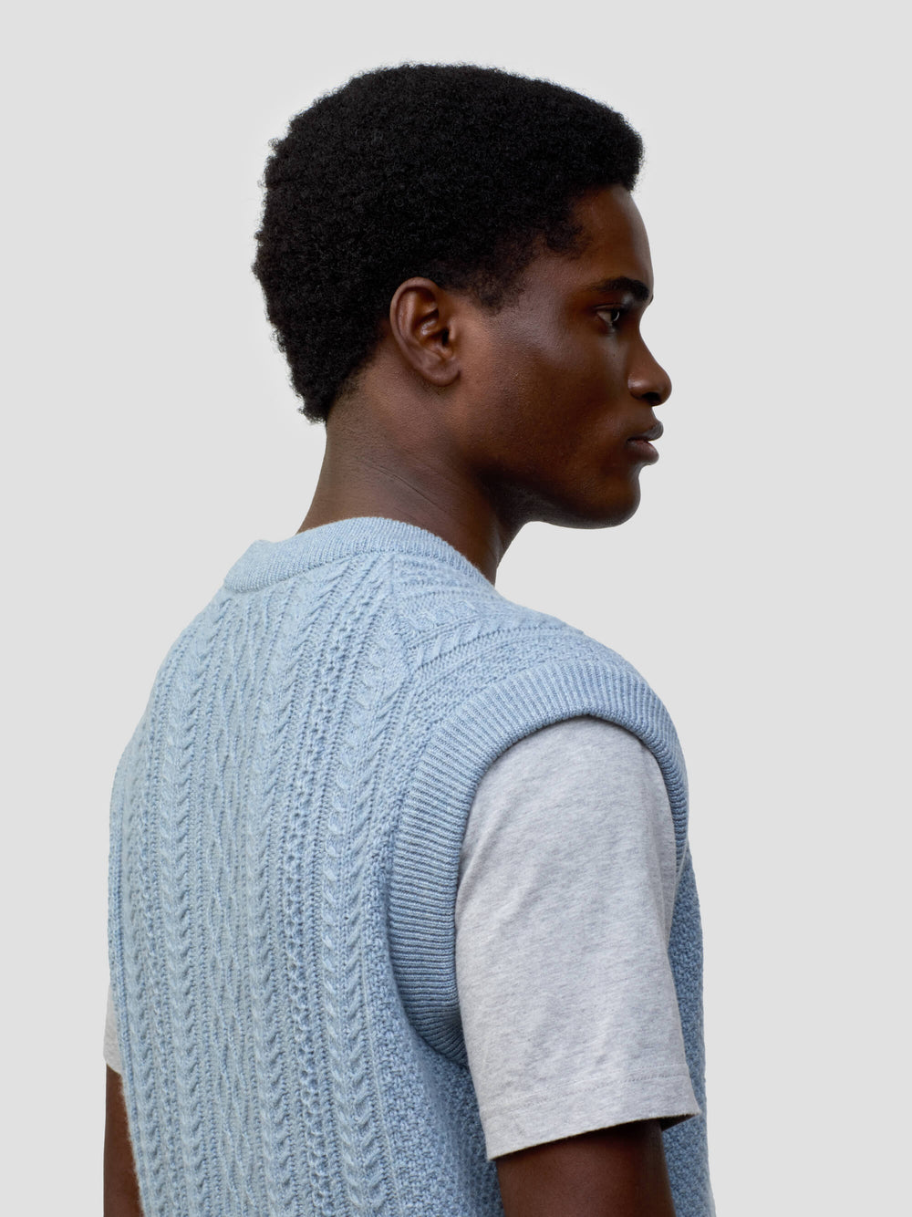man wearing an arran cable knit blue vest over a grey tshirt on a grey background