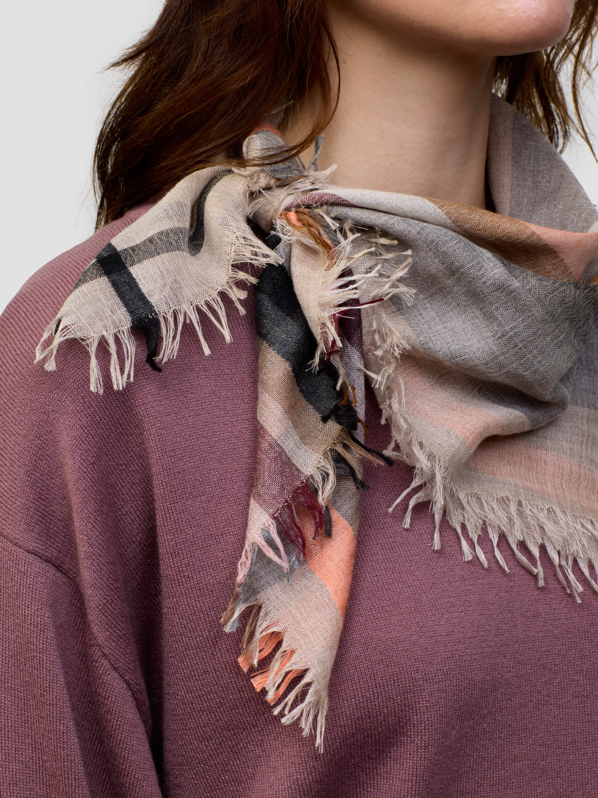 woman wearing a pink cashmere sweater  beige patterned scarf on a grey background