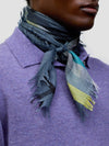 close up of a man wearing a purple cashmere poloshirt with blue, teal and yellow patterned scarf on a grey background
