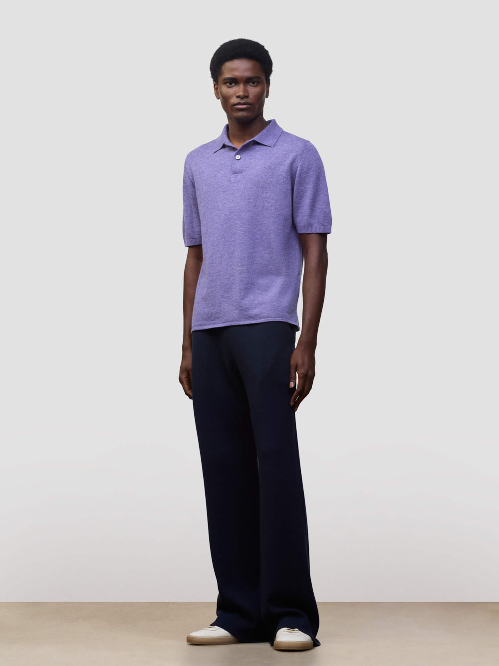 man wearing a short sleeve cashmere polo and navy trousers on a grey background