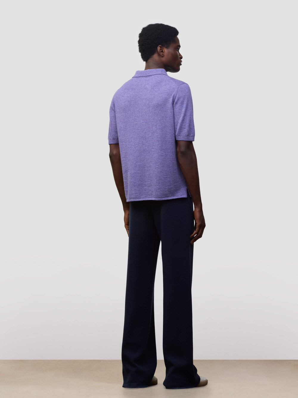 man wearing a short sleeve cashmere polo and navy trousers on a grey background