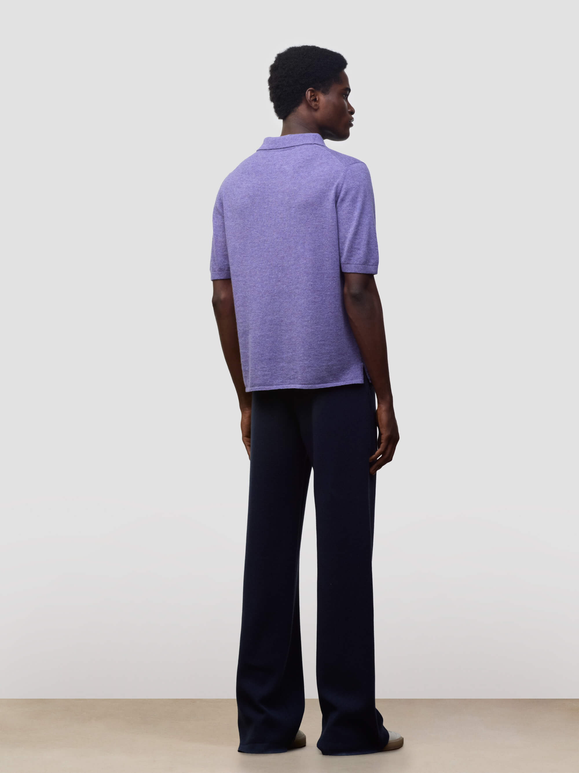 man wearing a short sleeve cashmere polo and navy trousers on a grey background