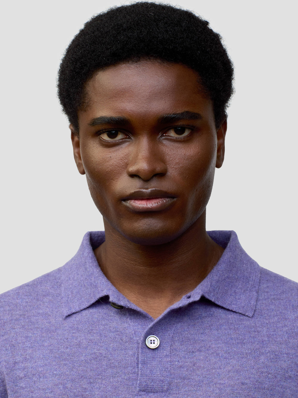 close up of a man wearing a short sleeve cashmere polo on a grey background