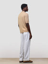 man wearing beige cashmere polo and white trousers on a grey background