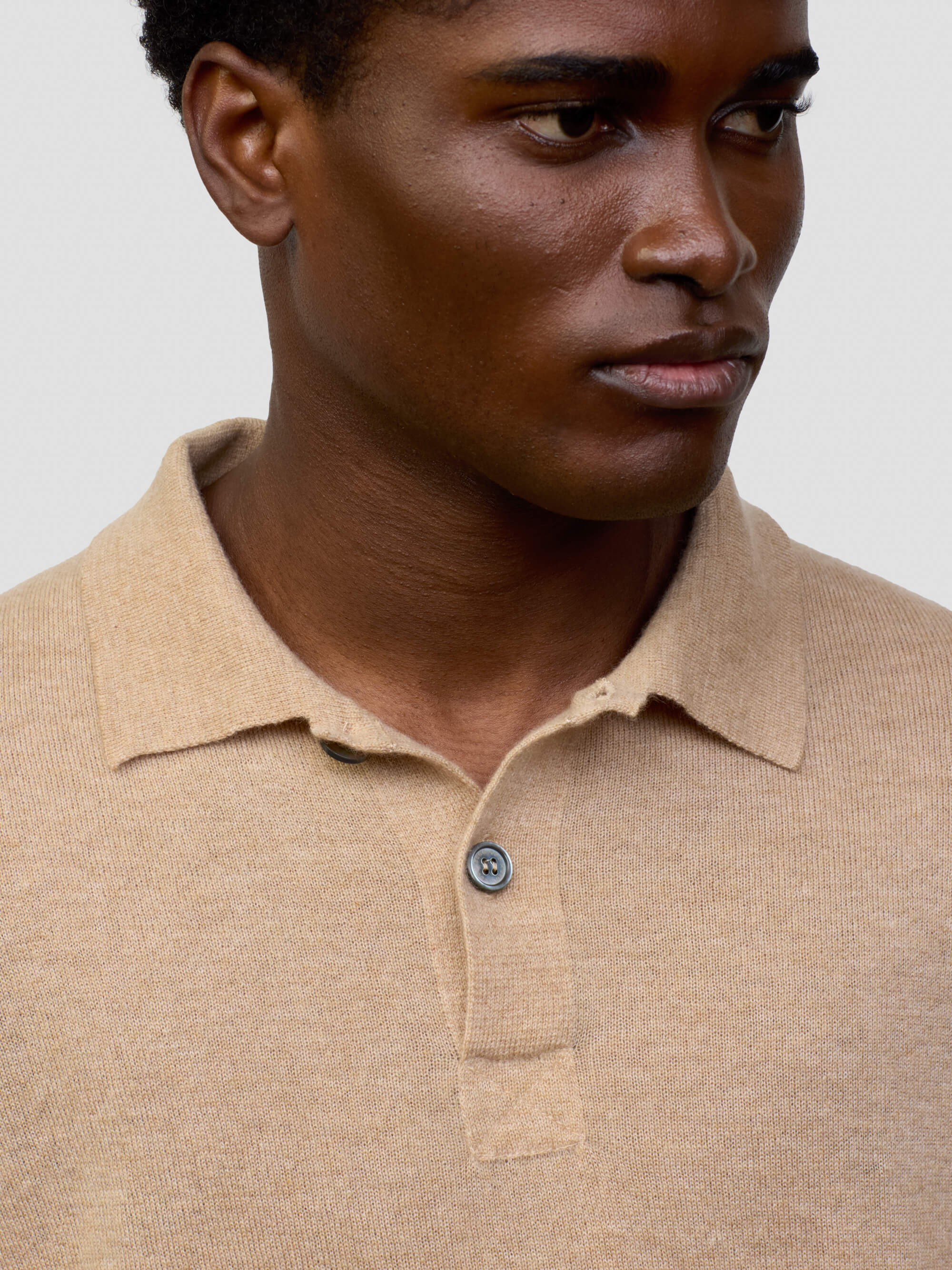 collar and button detail of a man wearing beige cashmere polo on a grey background