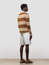 man wearing a striped brown and beige cashmere rugby shirt with white shorts on a grey background