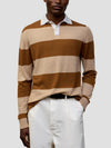 man wearing a striped brown and beige cashmere rugby shirt with white shorts on a grey background