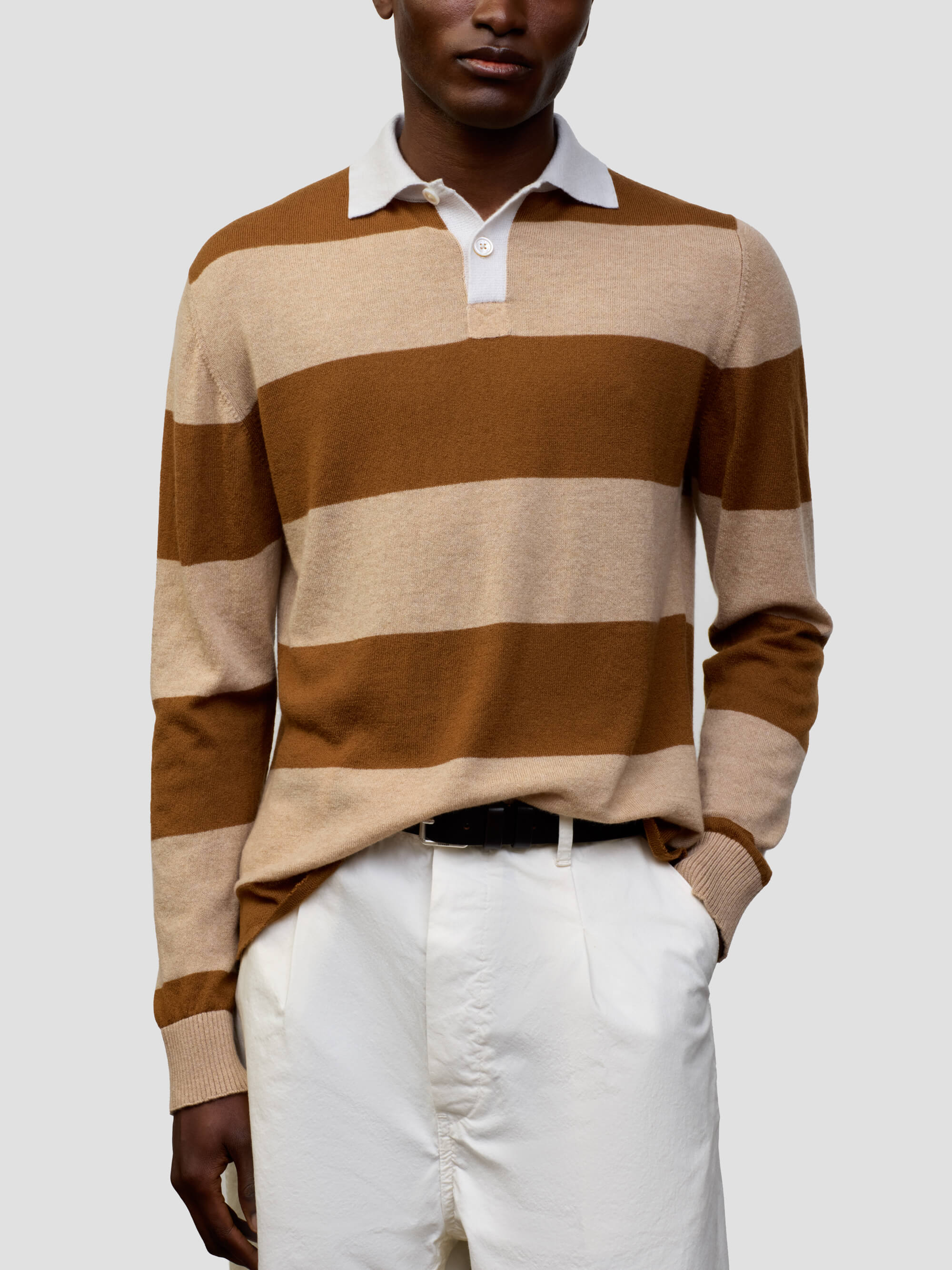 man wearing a striped brown and beige cashmere rugby shirt with white shorts on a grey background