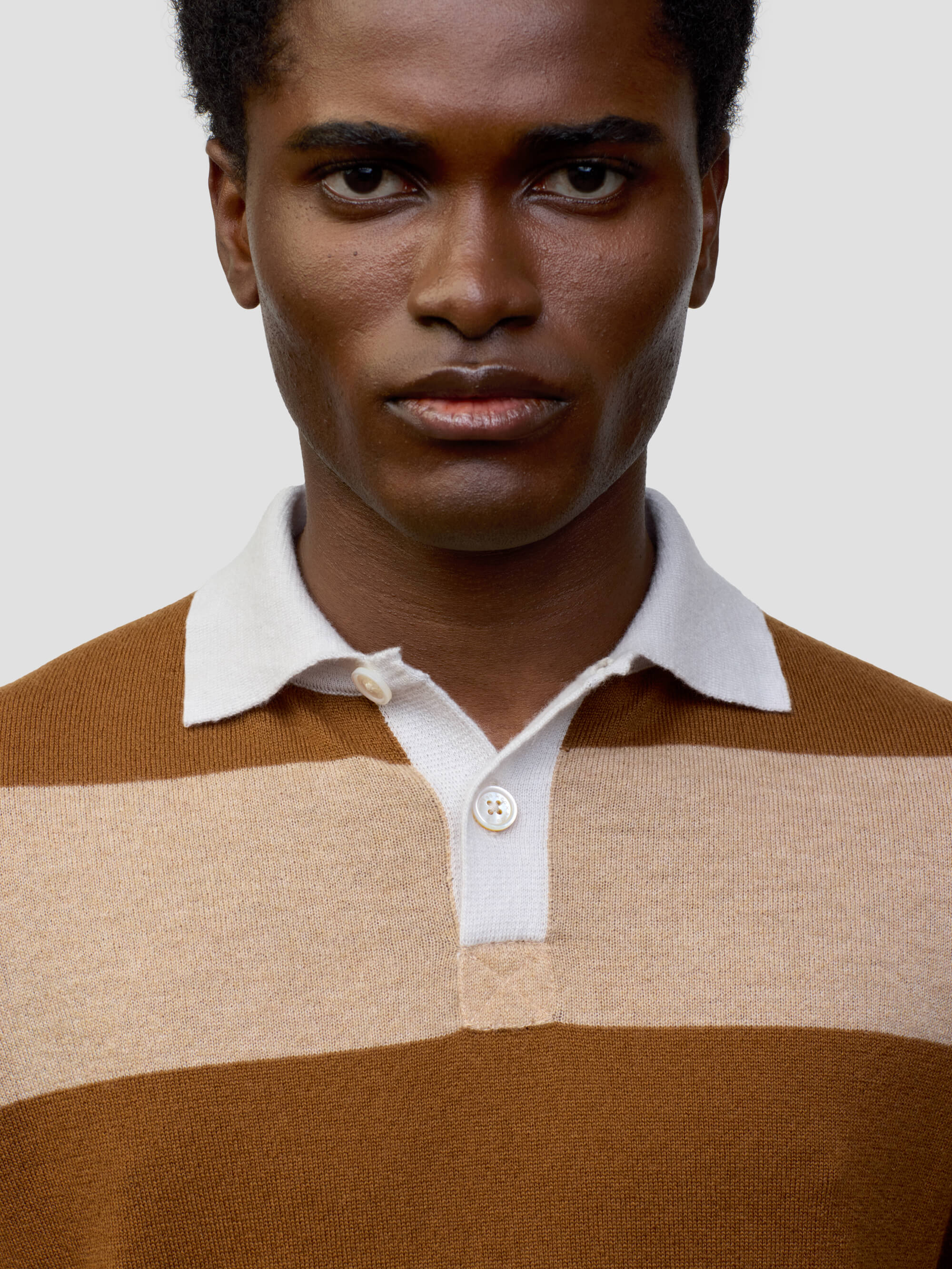 man wearing a striped brown and beige cashmere rugby shirt on a grey background