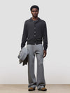 Person wearing a dark gray button-up cashmere cardigan over a gray sweater with light gray pants and holding a grey jacket on a white background