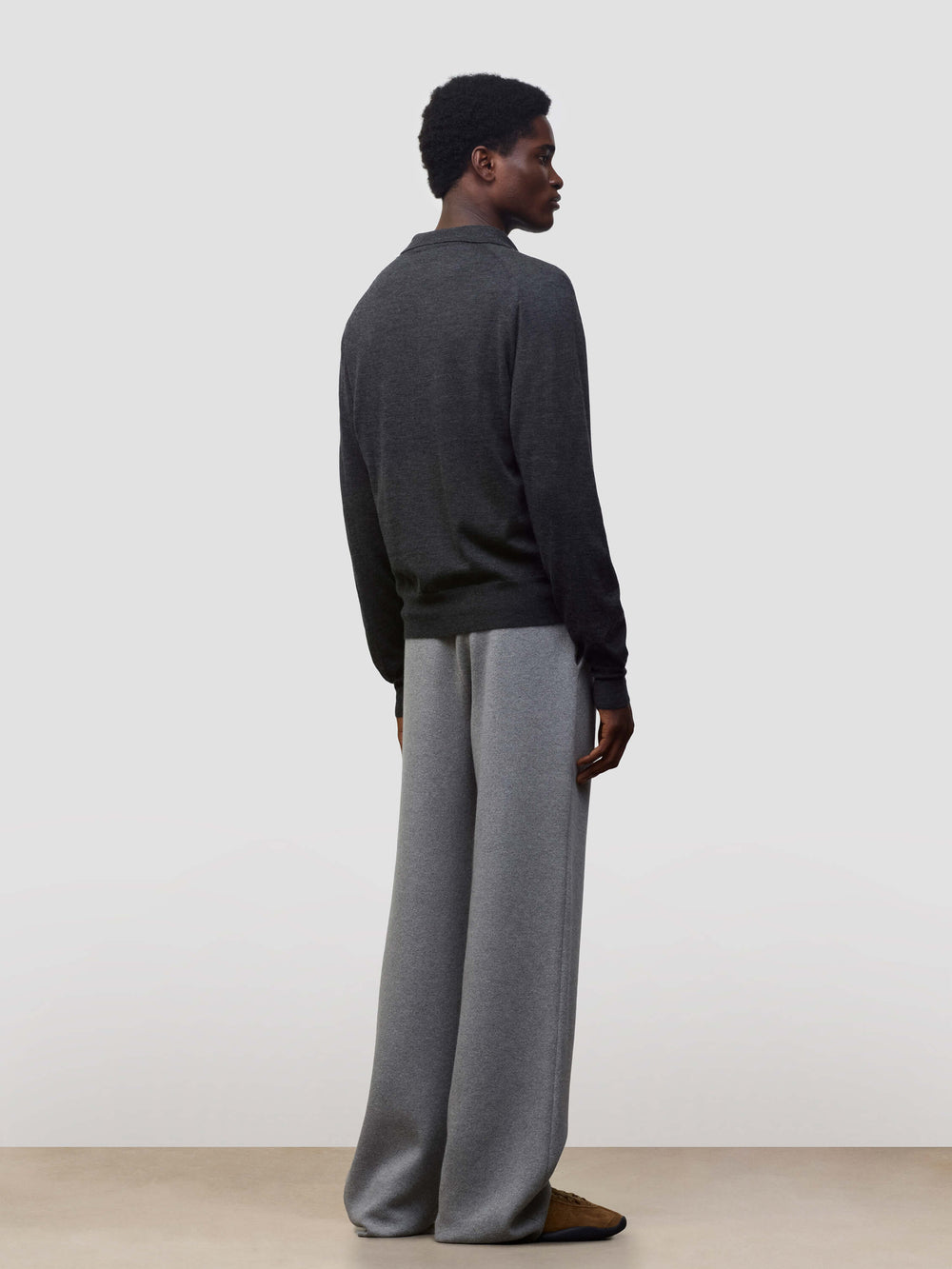Person wearing a dark gray button-up cashmere cardigan over a gray sweater with light gray pants on a white background