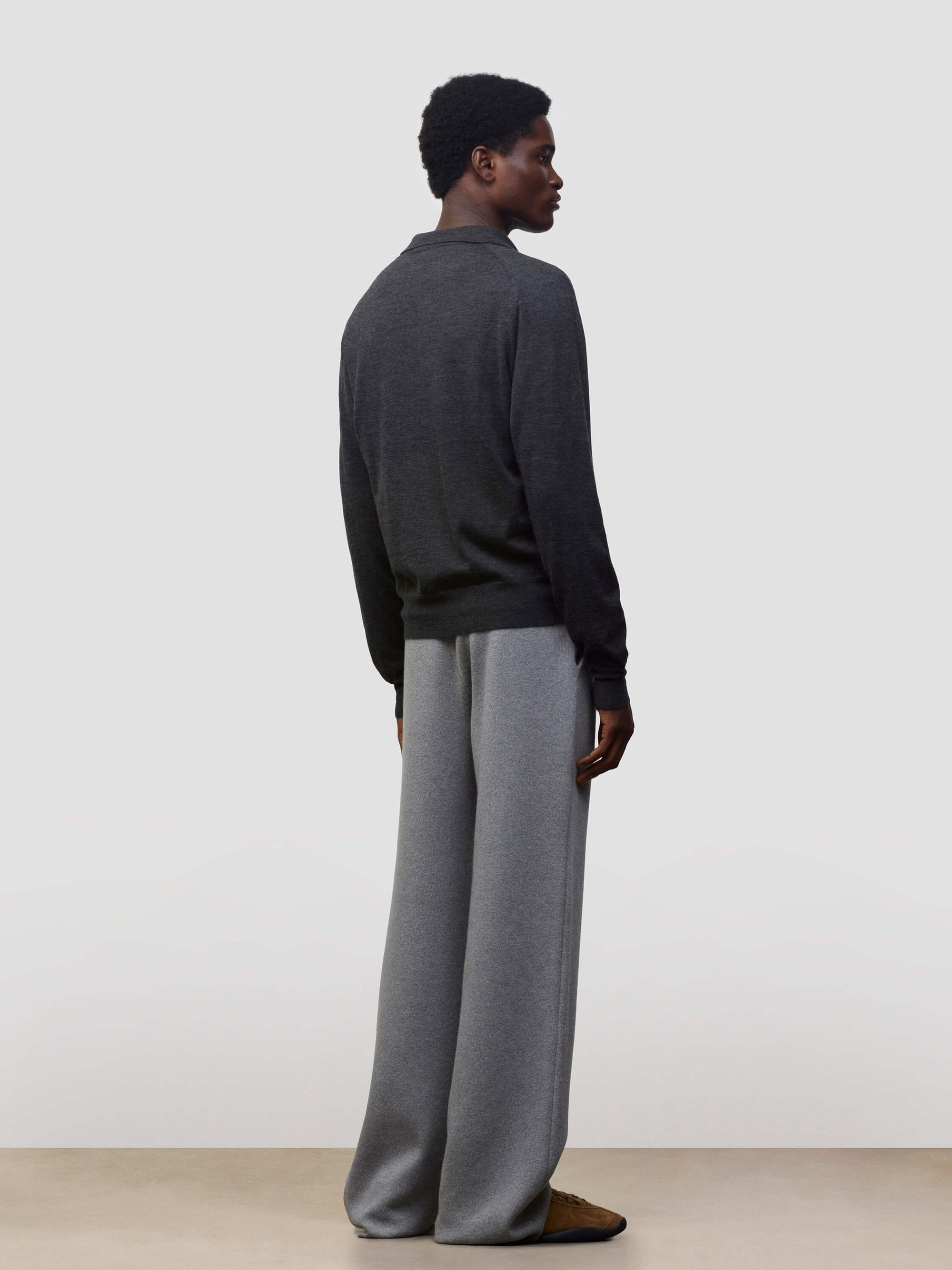 Person wearing a dark gray button-up cashmere cardigan over a gray sweater with light gray pants on a white background