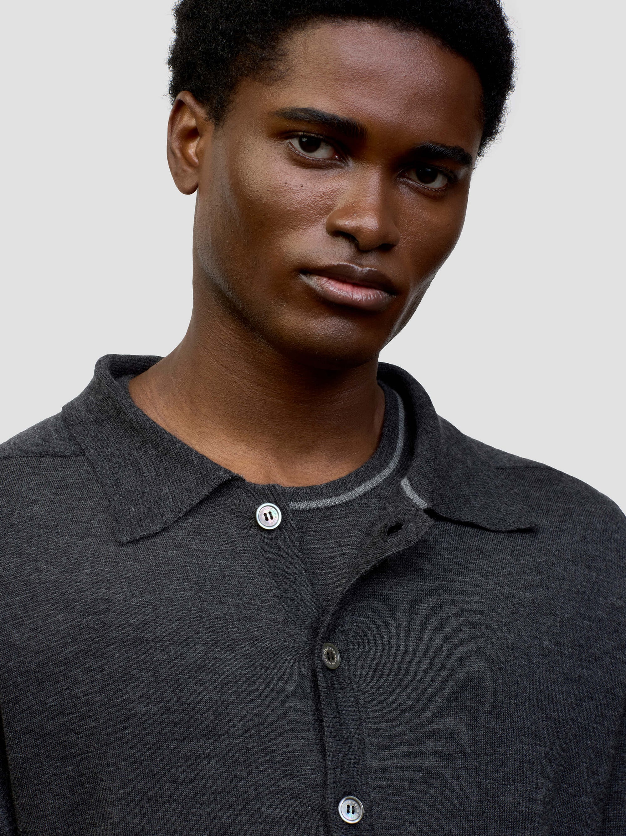 Person wearing a dark gray button-up cashmere cardigan over a gray sweater with light gray pants on a white background